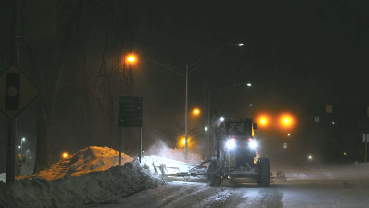 Snow plow clearing a road at night under orange streetlights