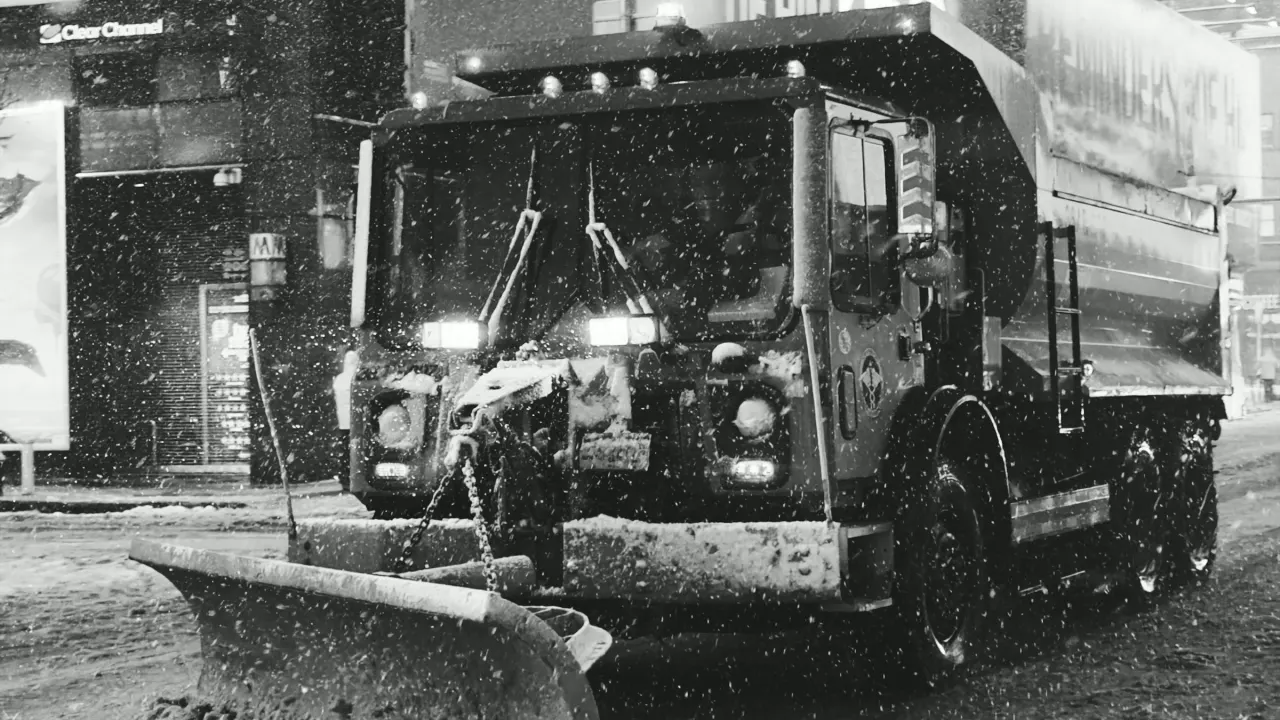 Plow truck with a front blade working in falling snow