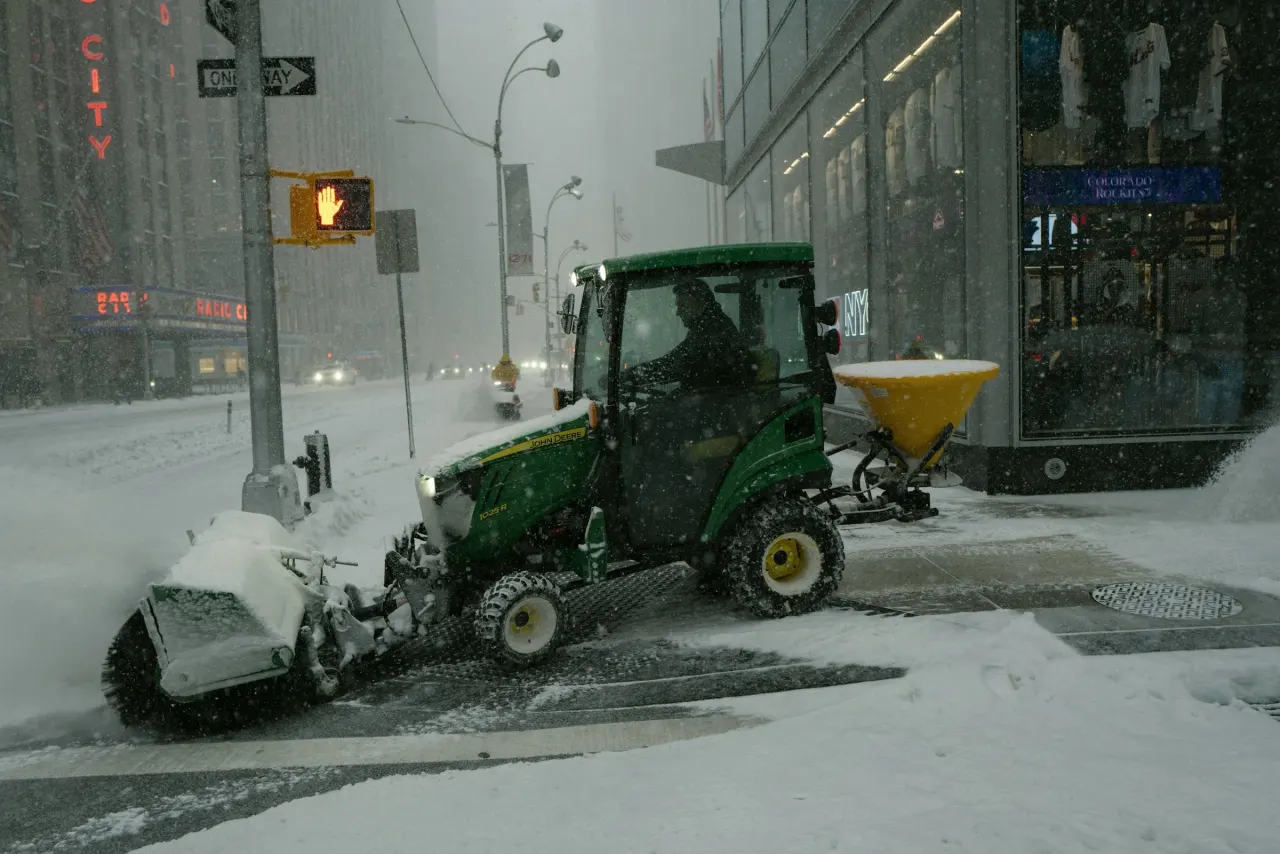 Tractor with a salt spreader treating a sidewalk in a snowstorm